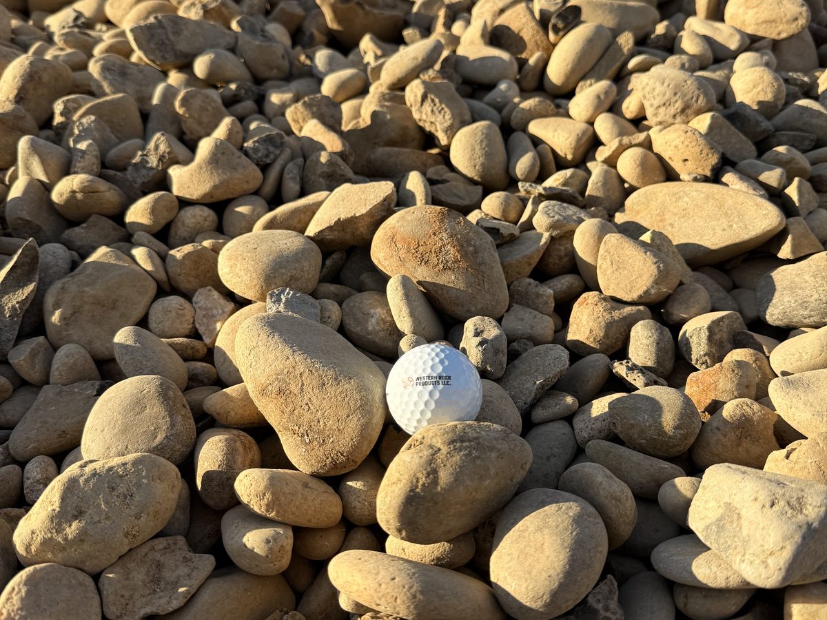 A stockpile of river rock cobble with a golf ball for scale