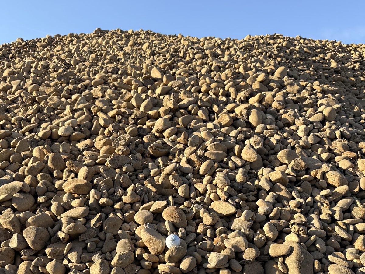 A large stockpile of river rock cobble under a blue sky